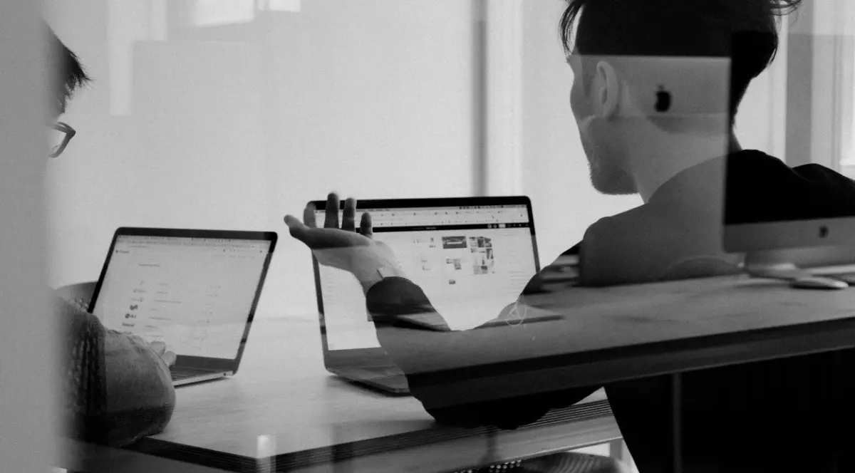 Two people working on laptops at a table (black and white photo)