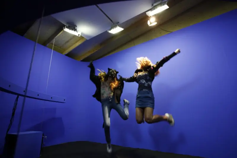 Two visitors jumping in mid-air in front of the blue backdrop of the Adidas Ghettorama installation