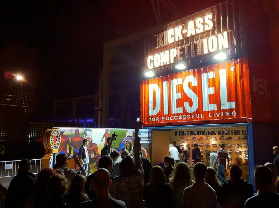 Crowd gathered at night in front of the Diesel Kick Ass Competition stand with a large lit Diesel sign
