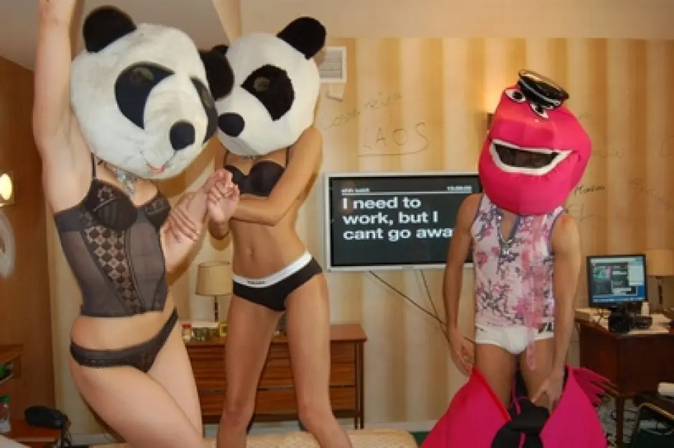 Two people wearing panda heads and another wearing a red mask, dancing in the motel room