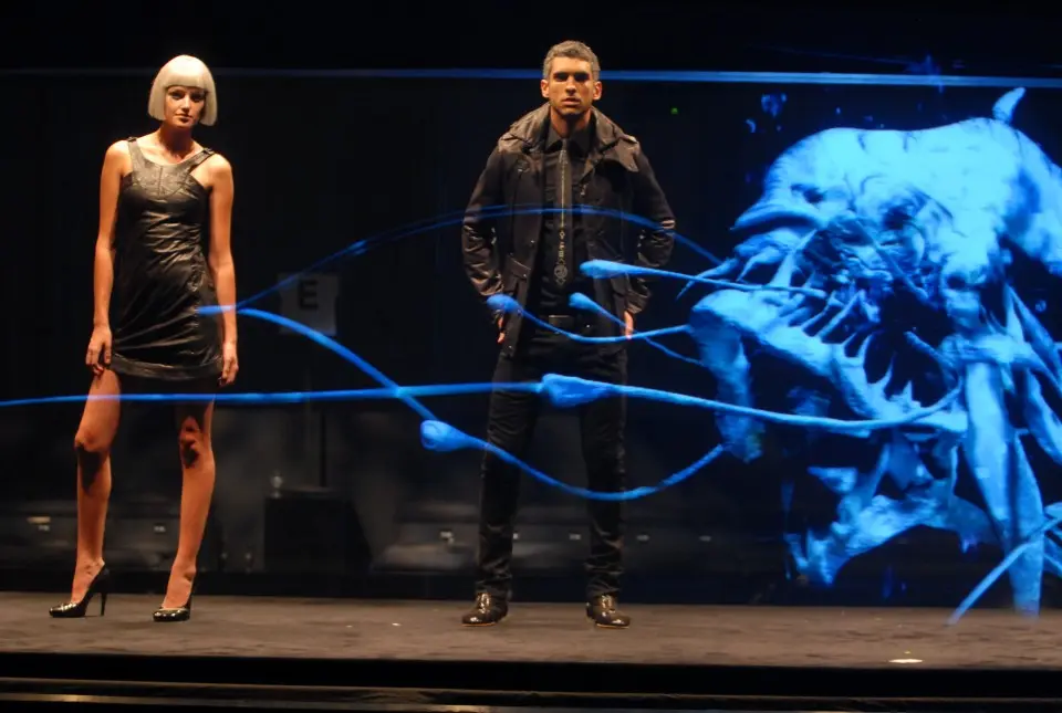Two models standing on the runway in front of a blue holographic sea creature