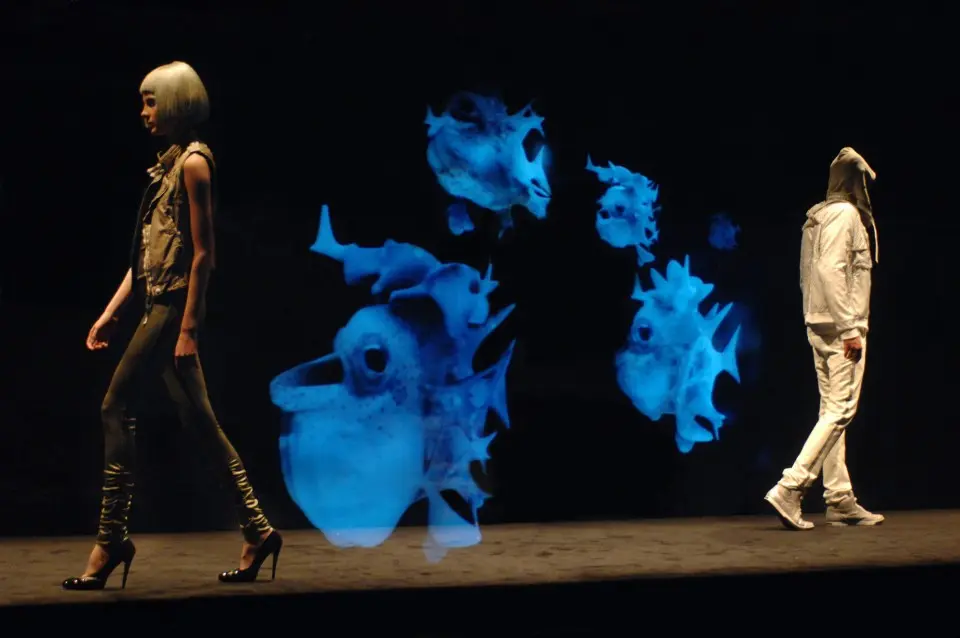 Models on the runway with holograms of blue fish and marine creatures floating behind them