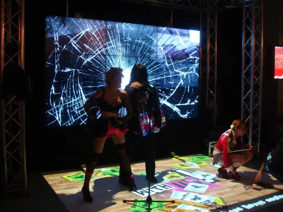 Two visitors standing in front of a large screen with a shattered glass effect, with colorful graphics projected on the floor