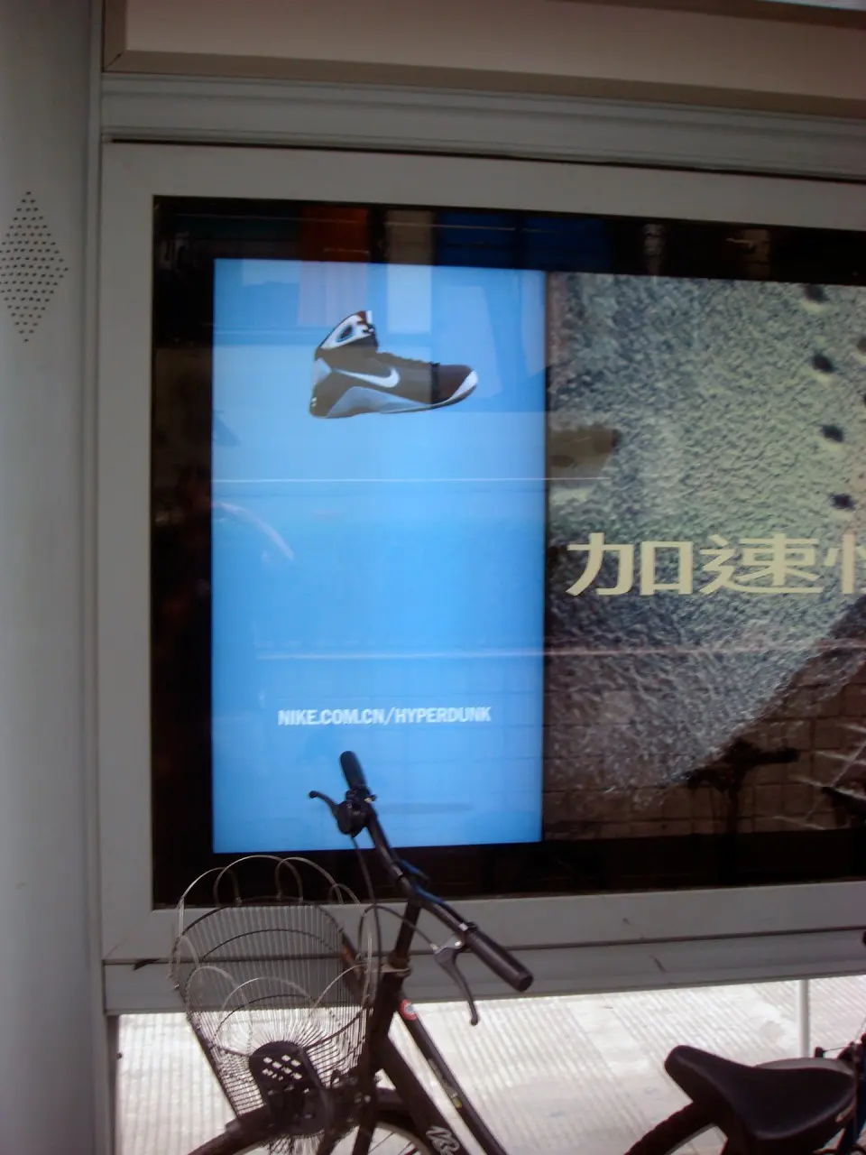 Close-up of the bus shelter screen with a blue Nike animation and a bicycle parked in front