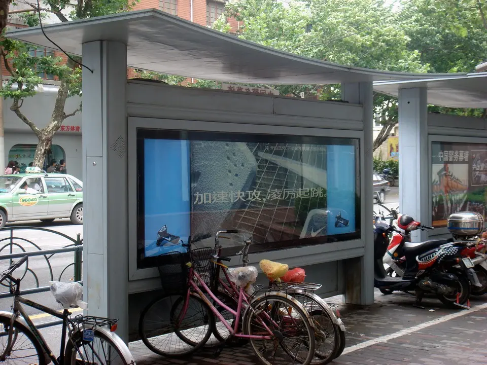 Nike bus shelter with an interactive screen and a woman walking by on a tree-lined Shanghai street